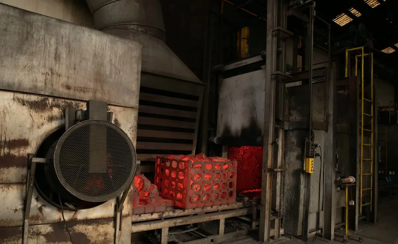 Red-hot castings in a basket exiting a heat treatment furnace